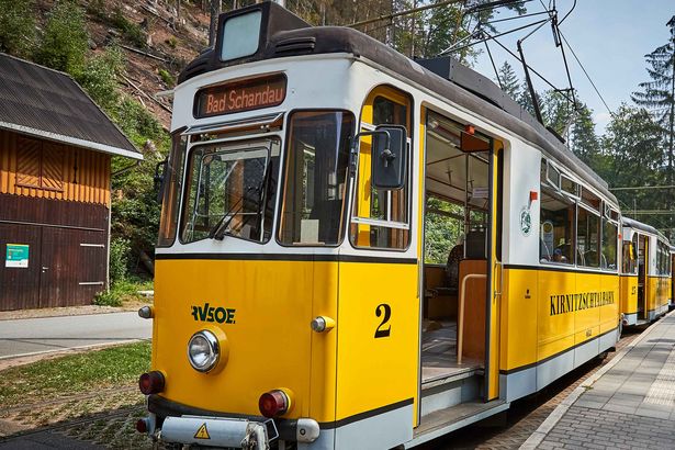 Kirnitzschtalbahn Straßenbahn im Nationalpark: Gelbe Bahn fährt durch grünen Wald, sonniges Sommerwetter.